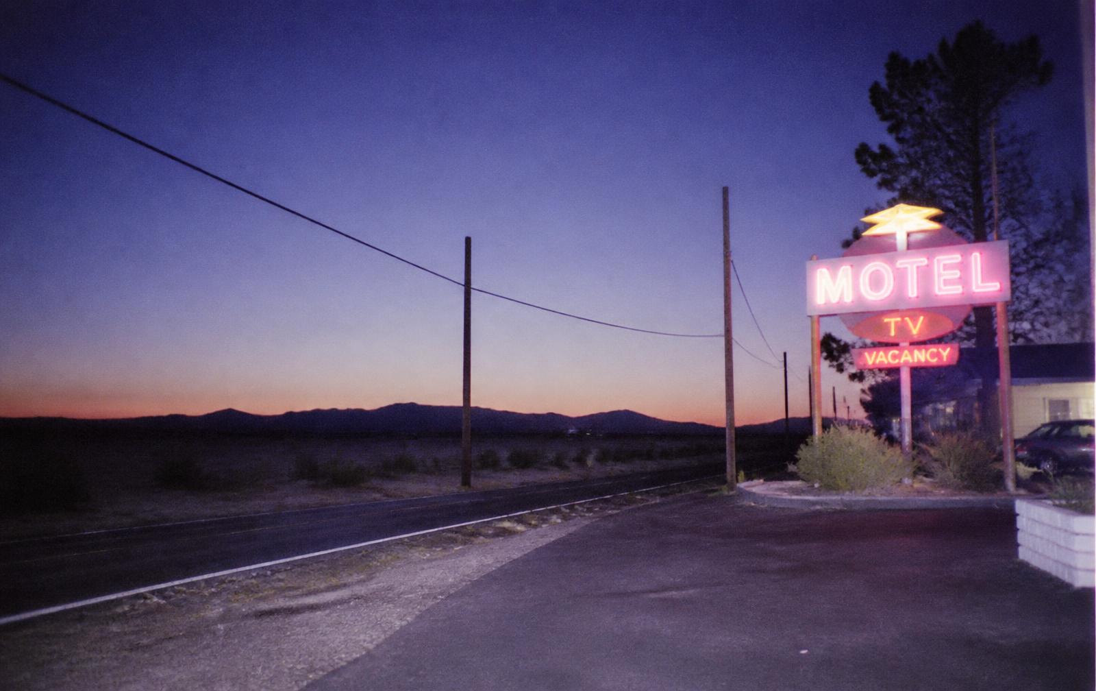 A neon motel sign lit at dusk beside an empty desert highway